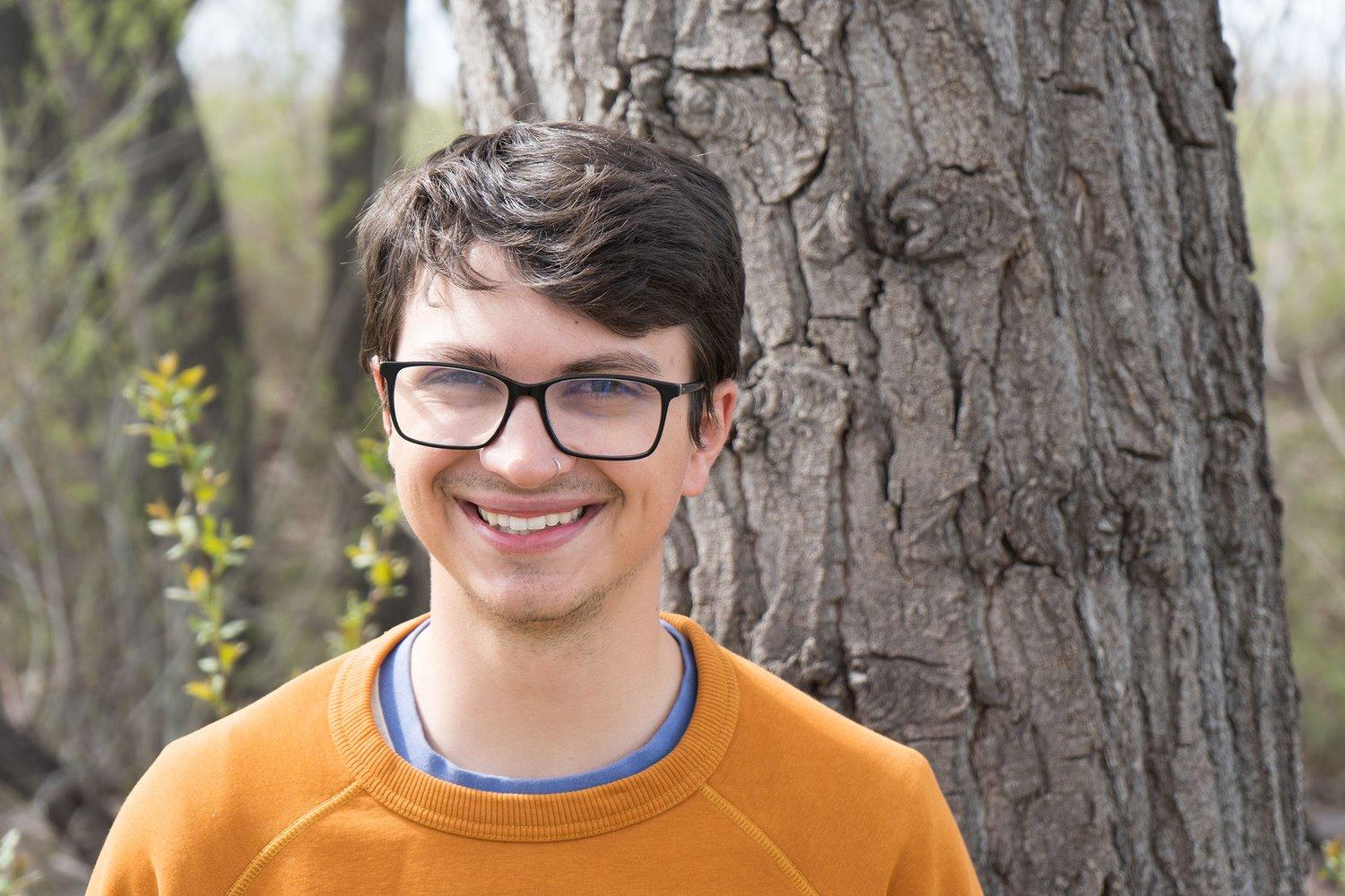 conservation forester Garrick Bateman stands smiling in front of a tree with an orange sweater