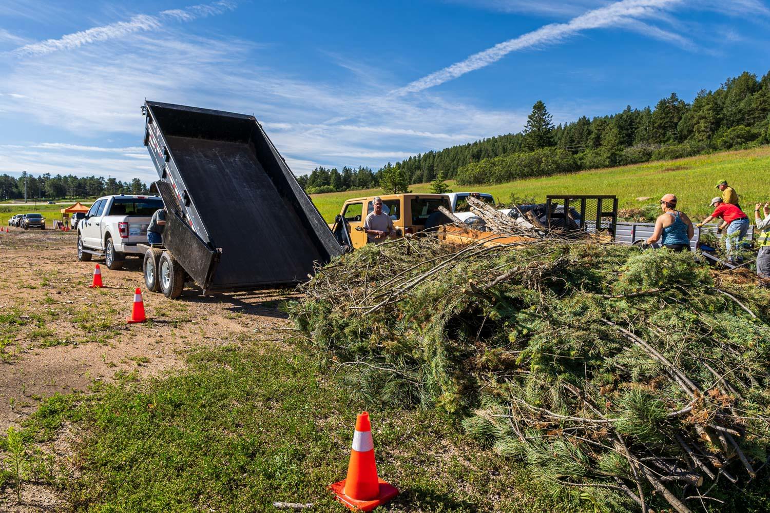 truck with trailer dumping tree debris and slash on the ground on a sunny day