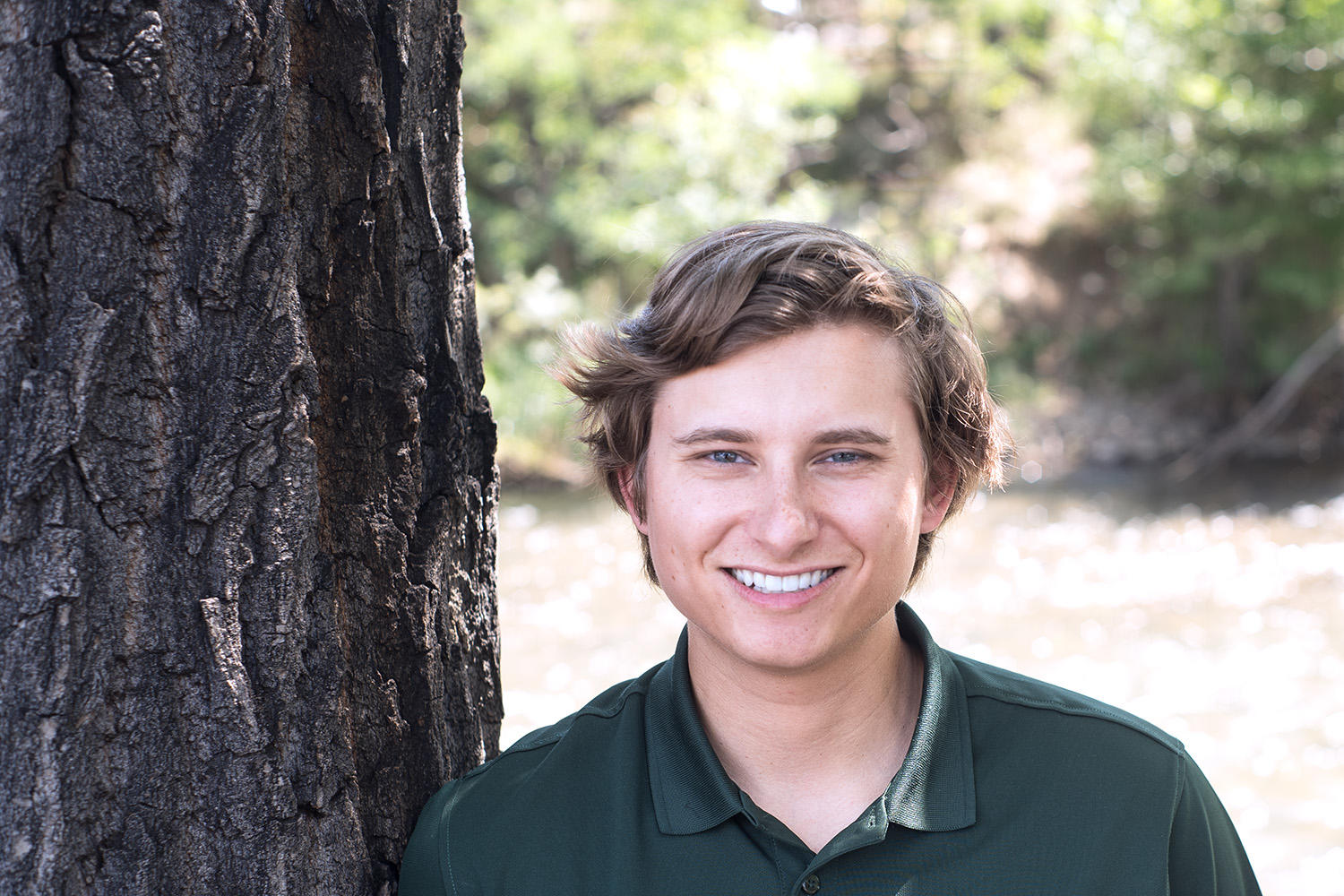 conservation forester Kyle Weber stands smiling next to a tree in a green polo shirt