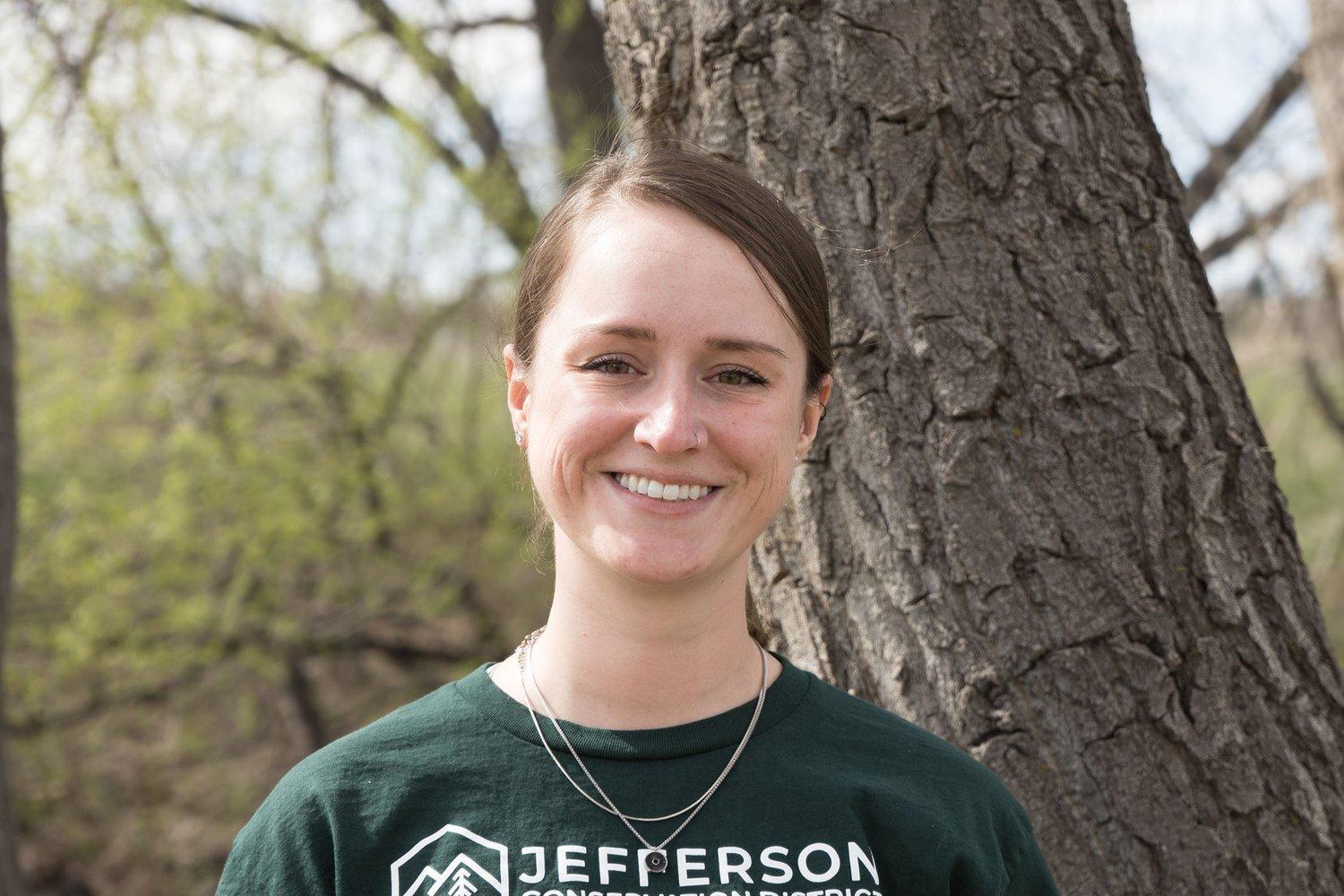 forest biomass coordinator Meagan Bragg stands smiling in front of a tree with a JCD shirt