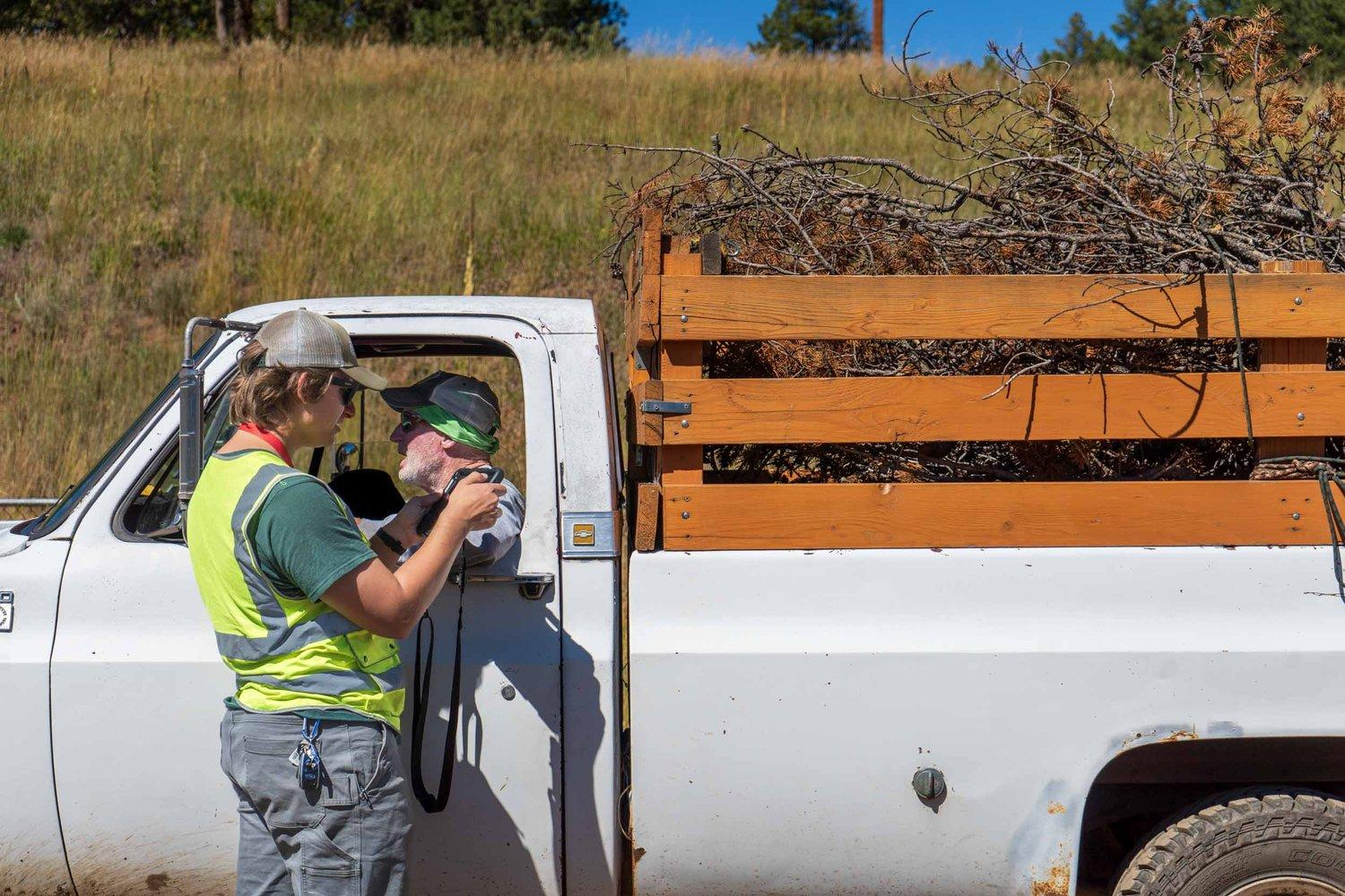 man in safety vest talking to a man in a pickup truck with branches in the back