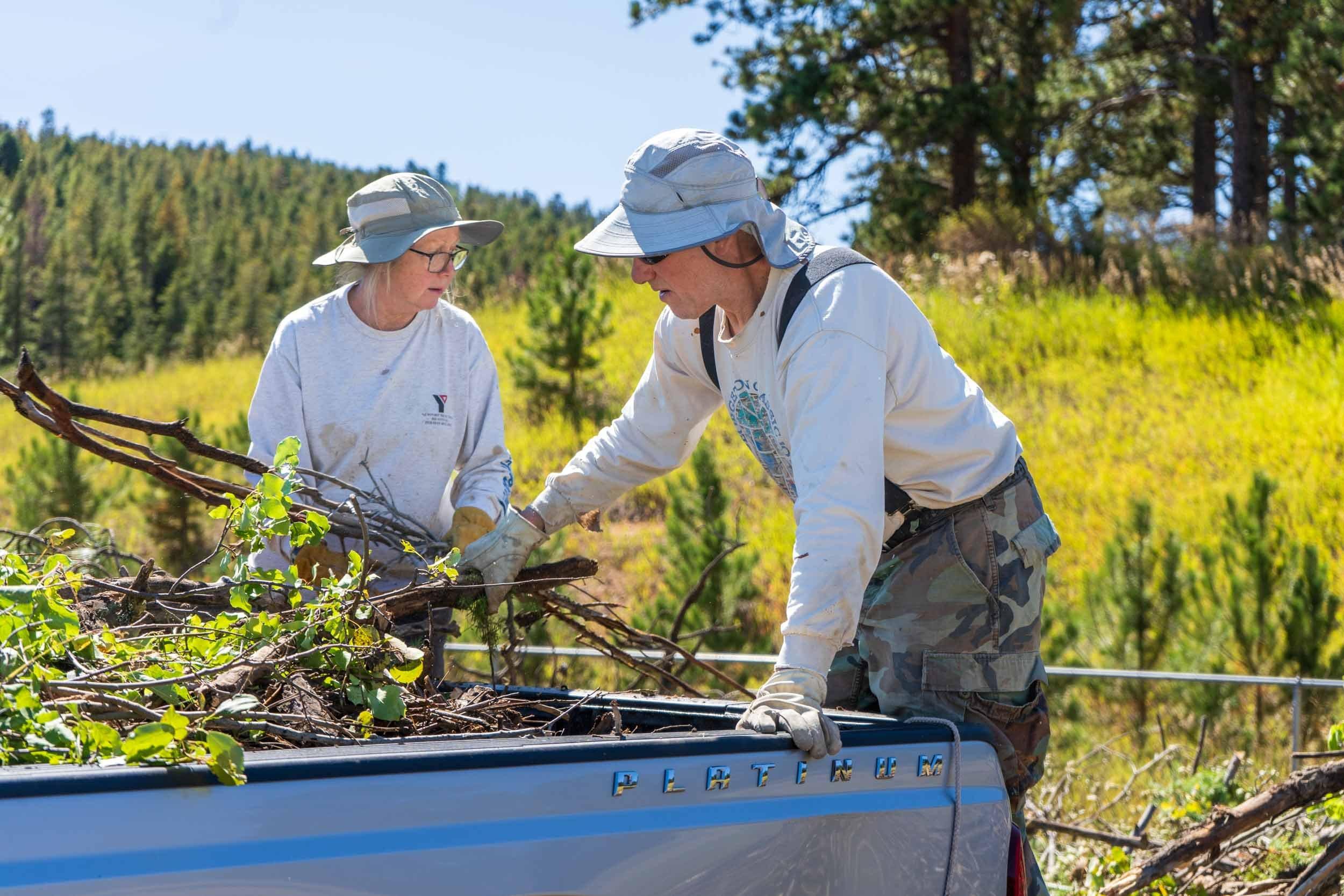 a couple with sun hats removing branches from their pickup truck on a sunny day