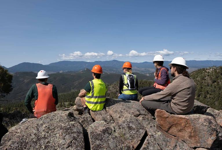 a group of conservation foresters sit on a ledge and look out at the Colorado mountains